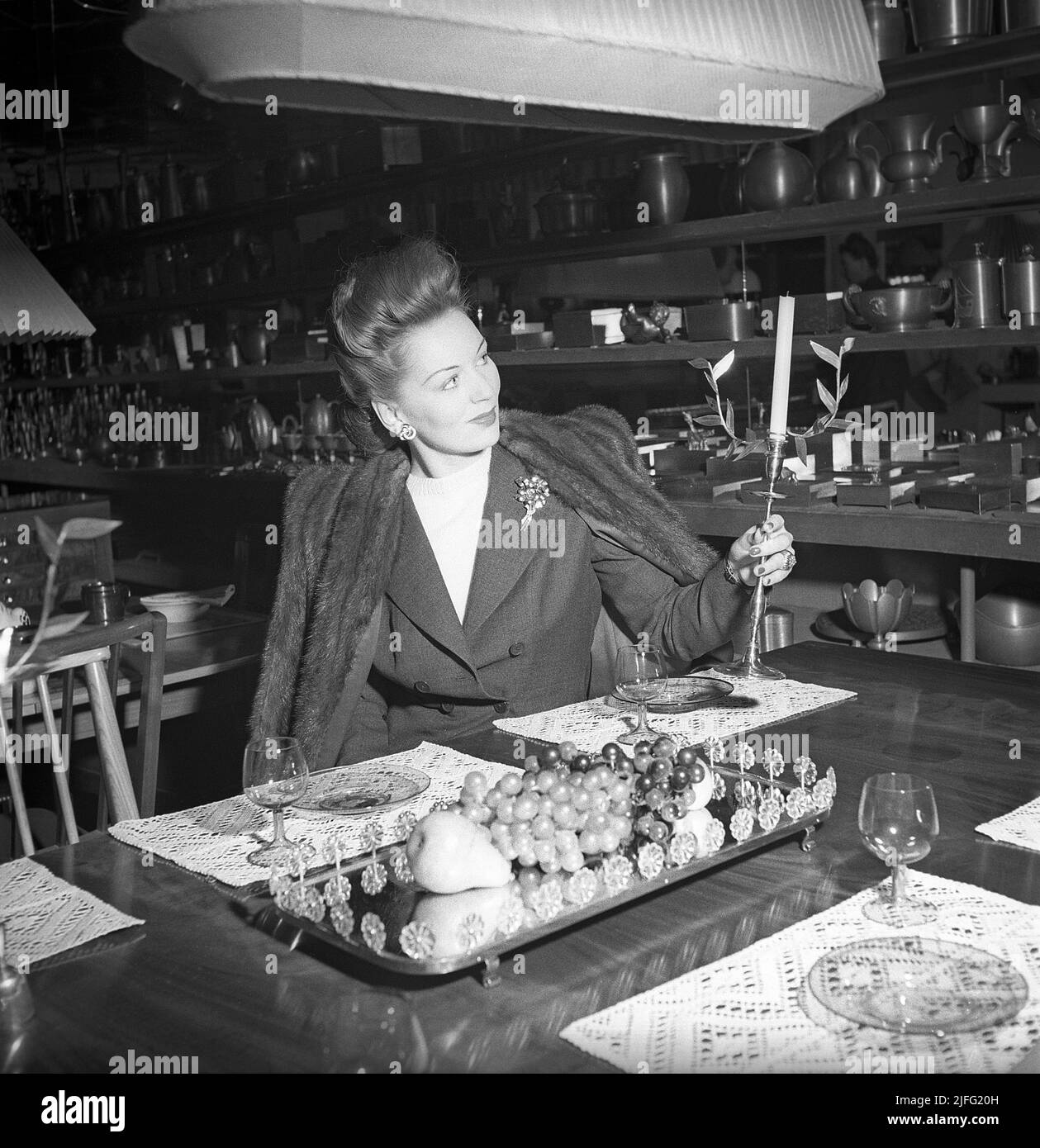 Compras en la década de 1940s. La actriz Greta Gynt, 1916-2000 en la tienda Svenskt tenn en Estocolmo fotografiado sosteniendo un palo de vela y con estanterías de artículos decorativos para la venta. La tienda es muy especializada y famosa por sus colecciones de diseño decorativo que se producen y que importa de todo el mundo. Svenskt tenn sigue en actividad (2022) Suecia 1946 ref X122-1 Foto de stock