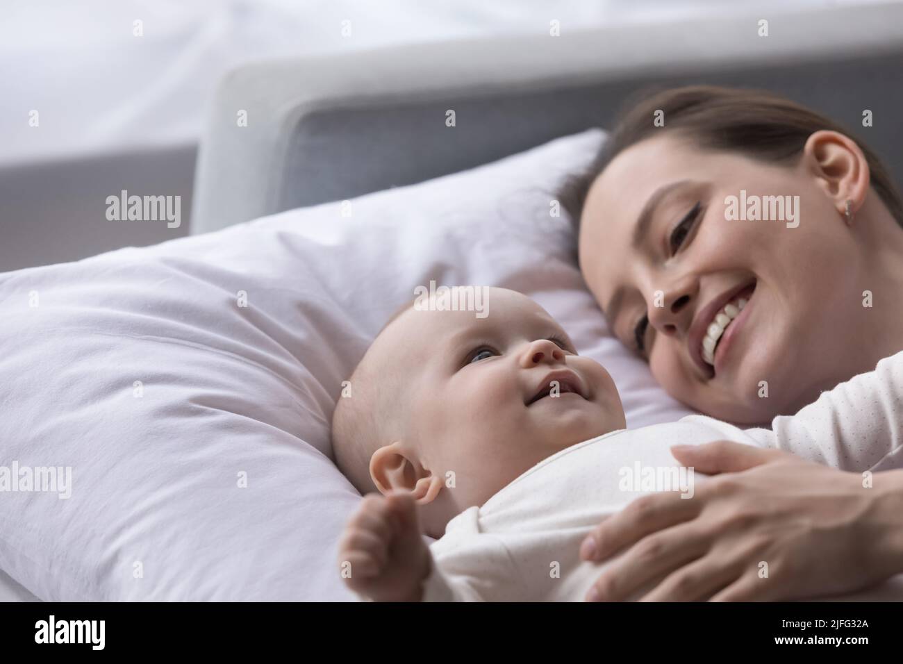 Bebé y madre acostados en la almohada sintiéndose refrescados mirando feliz Foto de stock