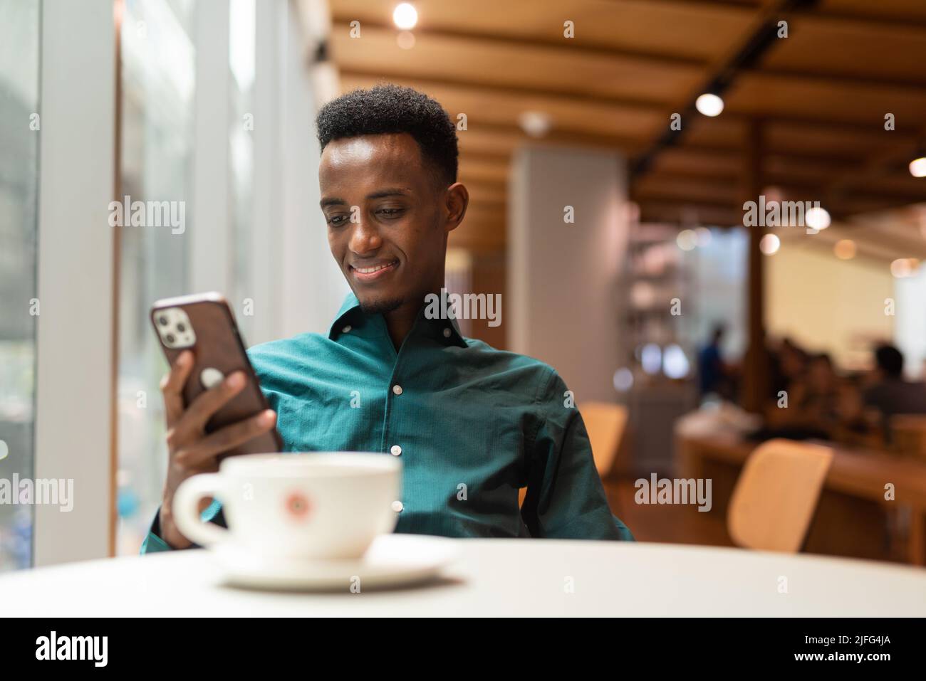 Hermoso joven negro en la cafetería usando el teléfono Foto de stock
