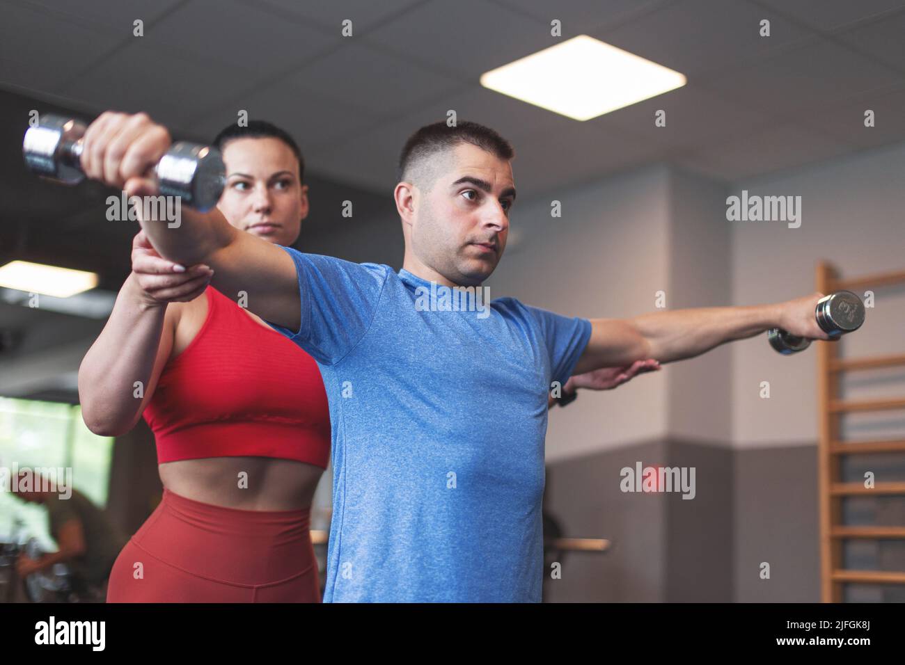 Mujer entrenador personal caucásica que sostiene el codo de los clientes durante el entrenamiento por las pesas Foto de stock