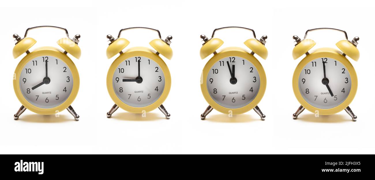 Concepto de despertar. Cuatro despertador amarillo vintage con recorte aislado sobre fondo blanco. Reloj despertador circular de metal con timbre de burbujas con hora variada. Foto de stock