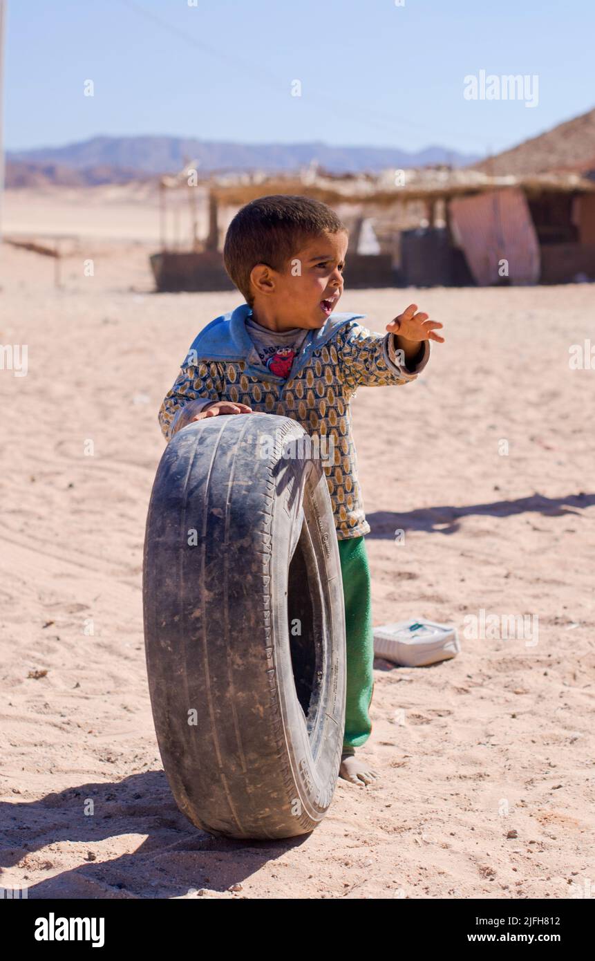 SHARM EL SHEIKH, EGIPTO - OCTUBRE 31 2014: Lindo niño egipcio se encuentra en el desierto sosteniendo un neumático desgastado. El niño juega sobre la arena contra la distancia Foto de stock