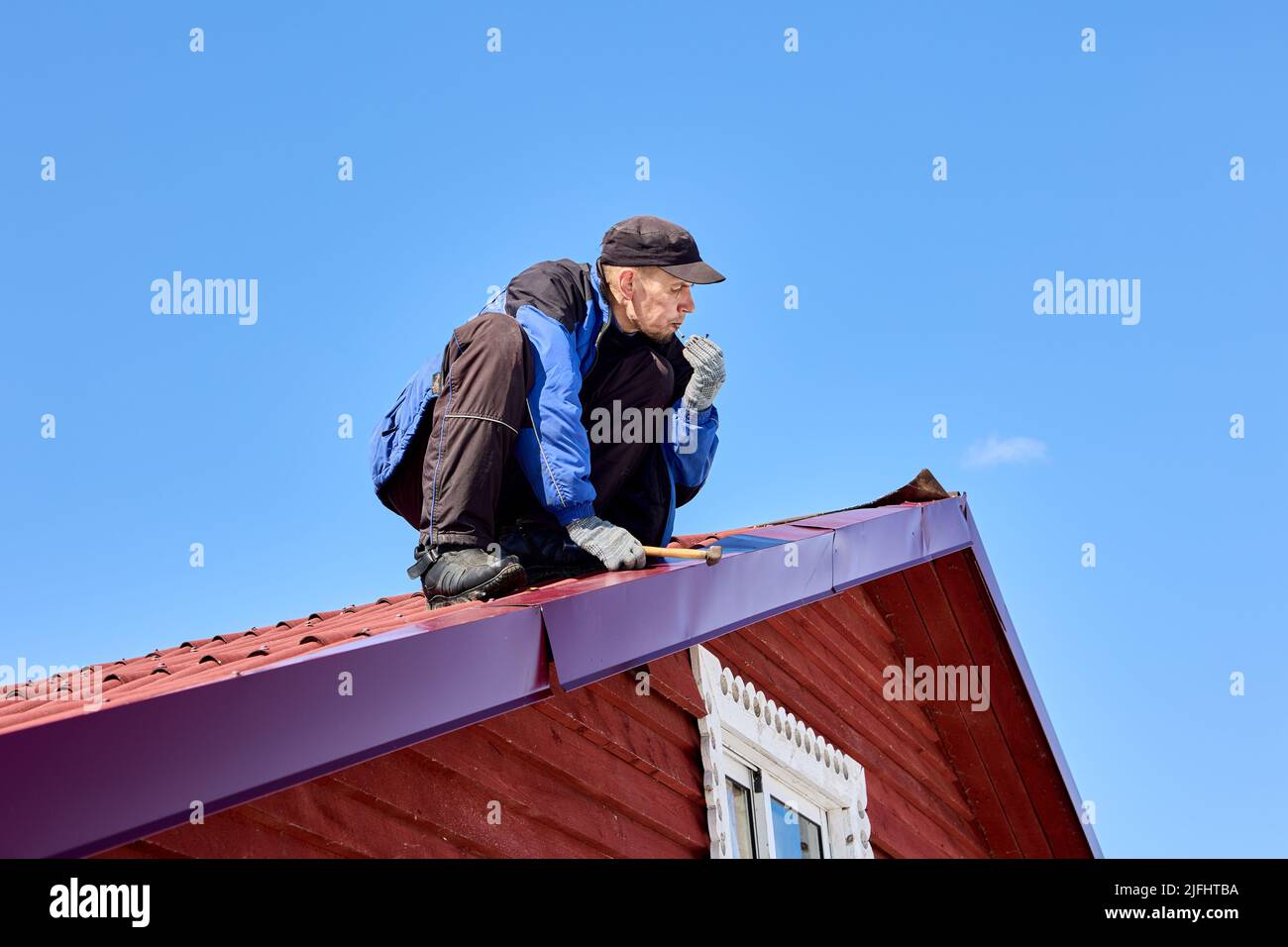 Clavando en el techo de hojalata Mientras techado, el trabajador usa un martillo para fijar el techo. Foto de stock