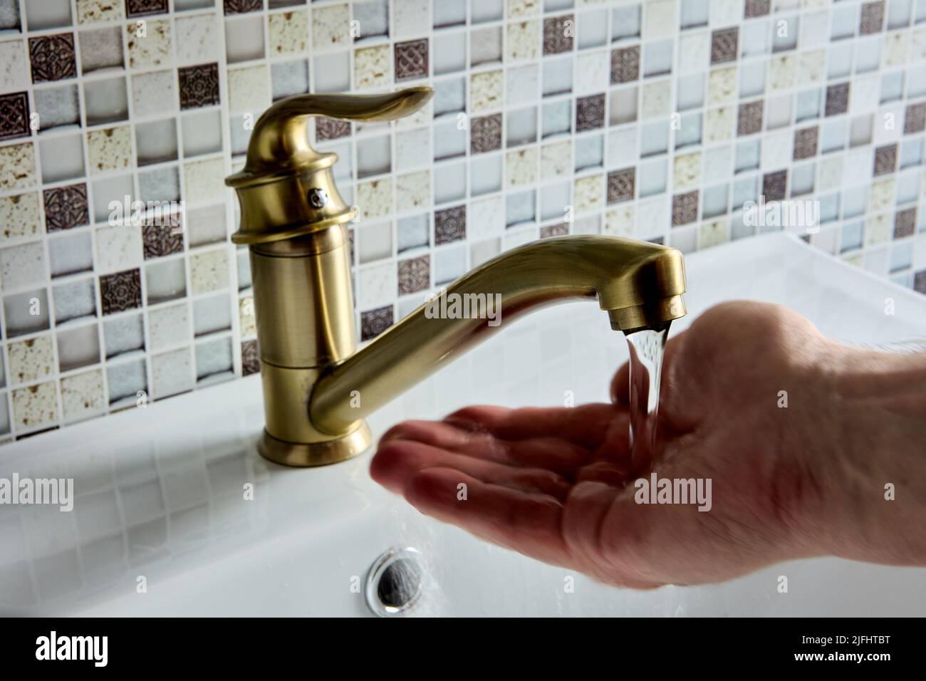 Grifo monomando de latón con palanca de codo simple en el baño, la mano está comprobando la temperatura del agua. Foto de stock