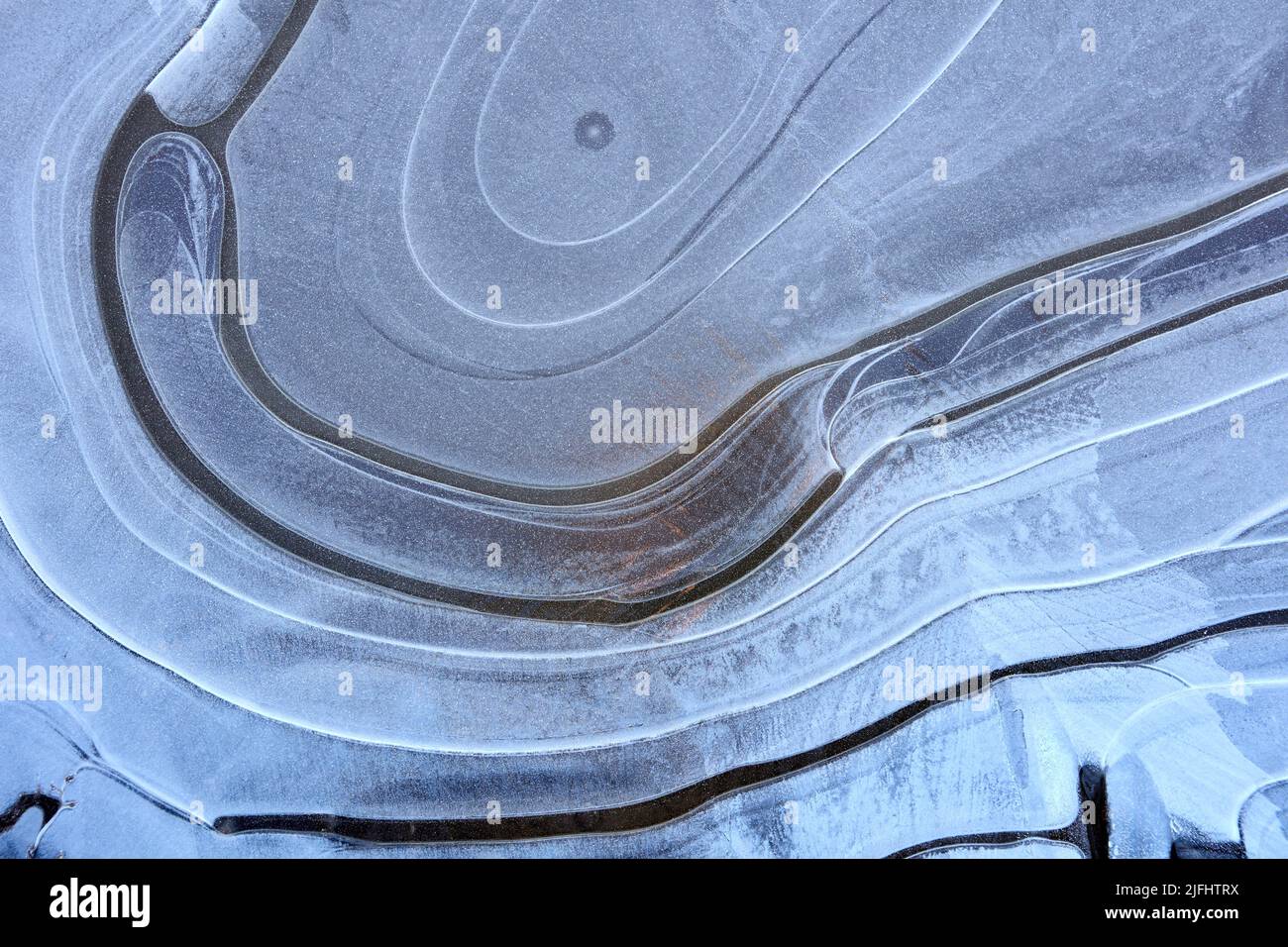 En la superficie de un charco congelado, patrón de líneas curvas. Foto de stock