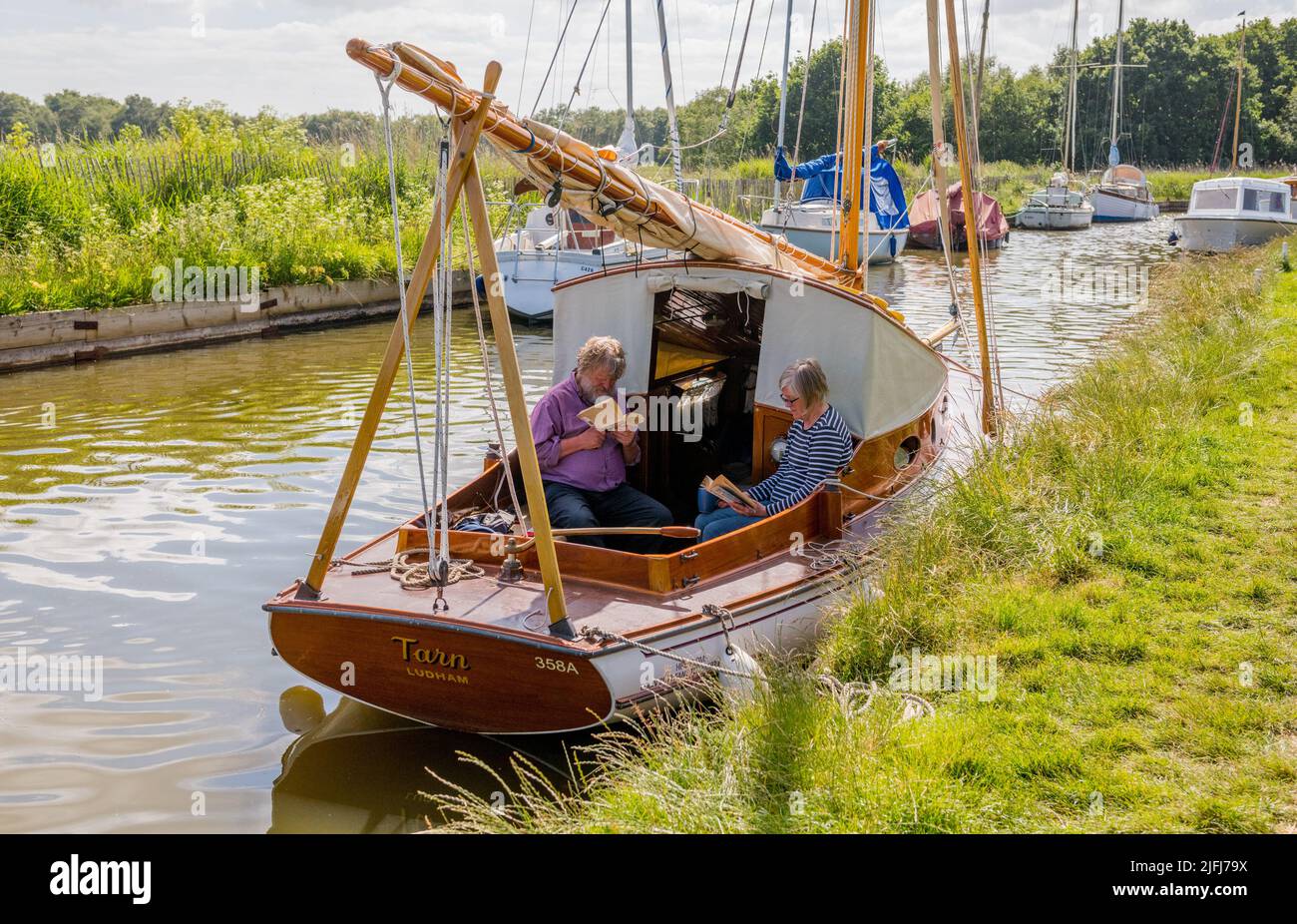 Pareja mayor amarrada en Horsley Mere y leyendo en un tradicional Norfolk Broads clásico velero. Foto de stock