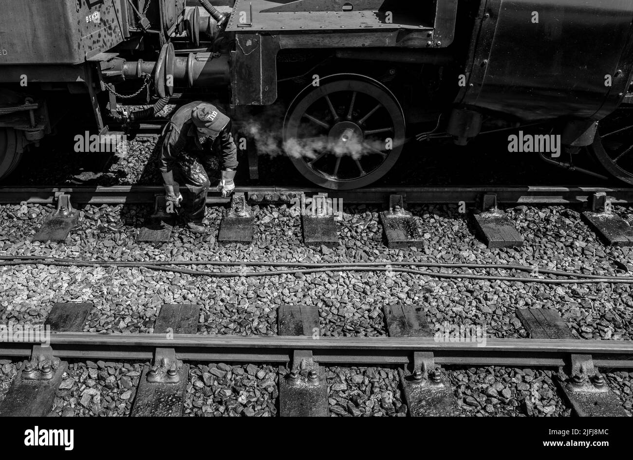 Trabajador del tren de vapor masculino que viene de debajo de un tren entre las ruedas Foto de stock