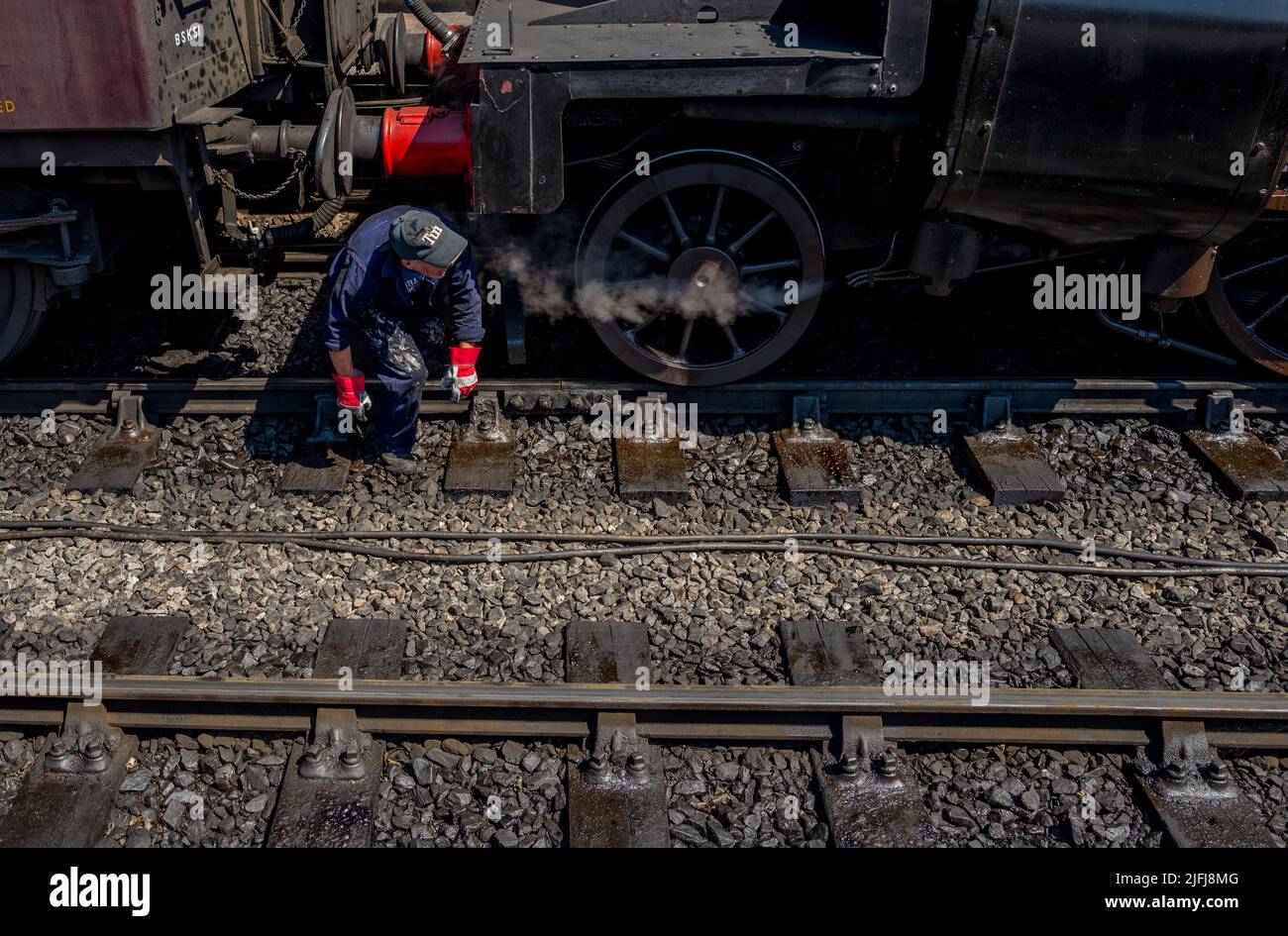 Trabajador del tren de vapor masculino que viene de debajo de un tren entre las ruedas Foto de stock