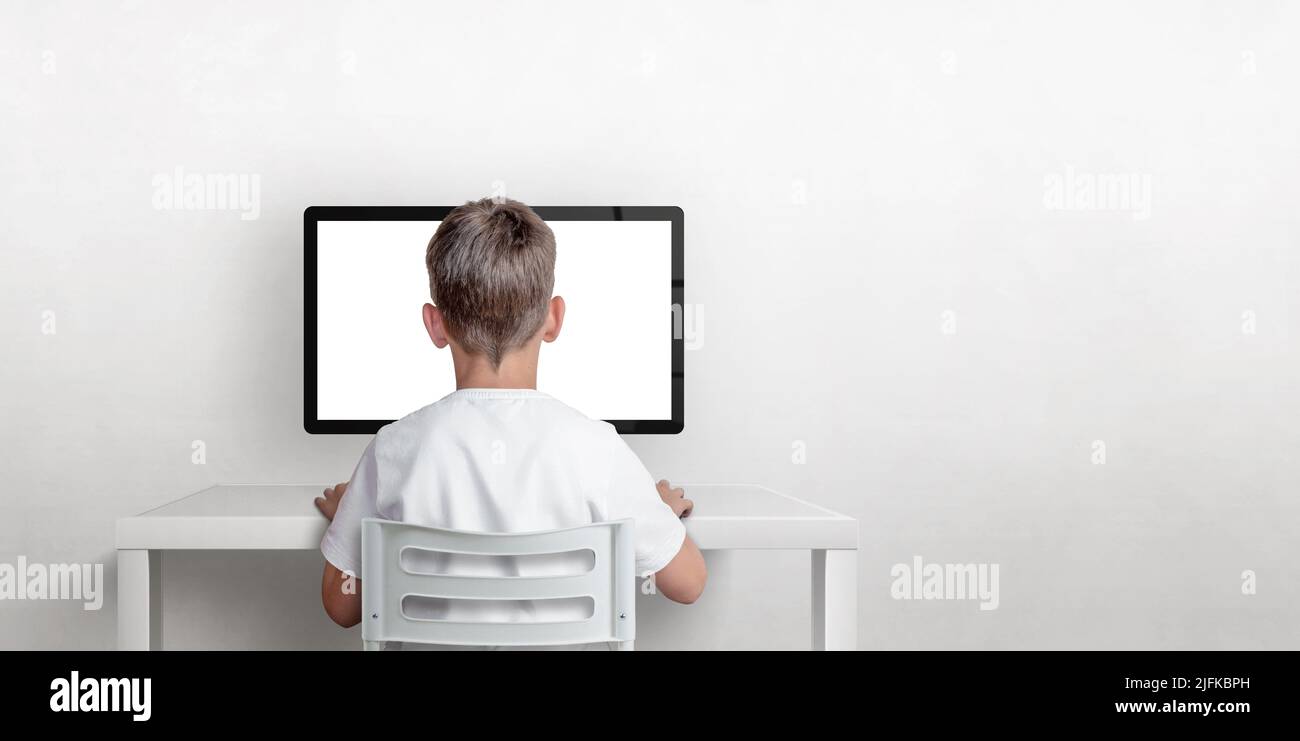 El muchacho está trabajando en la computadora, su espalda se da vuelta. Pantalla de ordenador aislada para mockup. Espacio de copia en la pared. El concepto de trabajo y aprendizaje Foto de stock