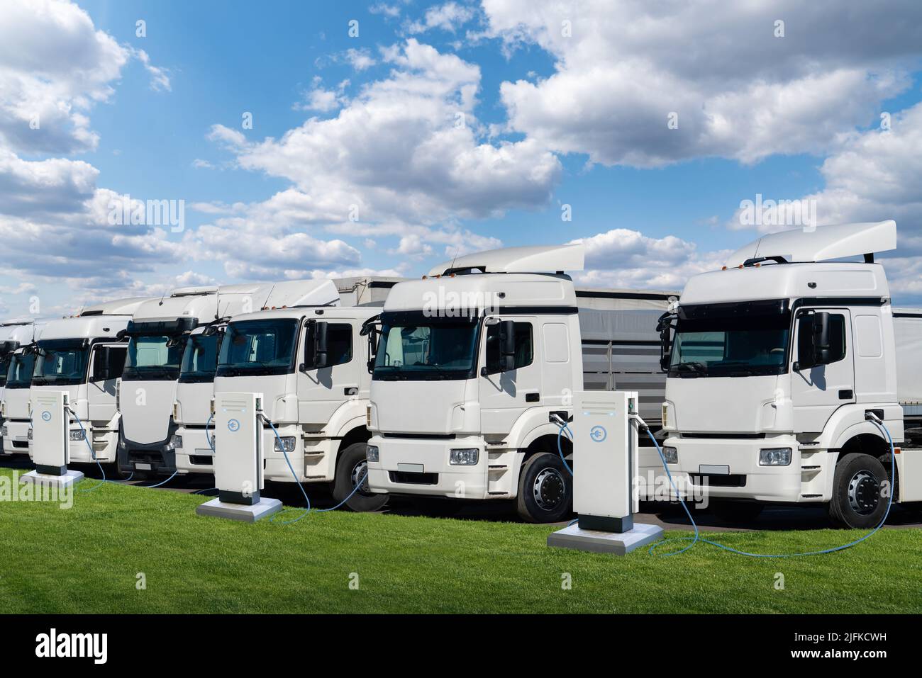 Fila de semi camiones eléctricos en estaciones de carga para vehículos eléctricos Foto de stock
