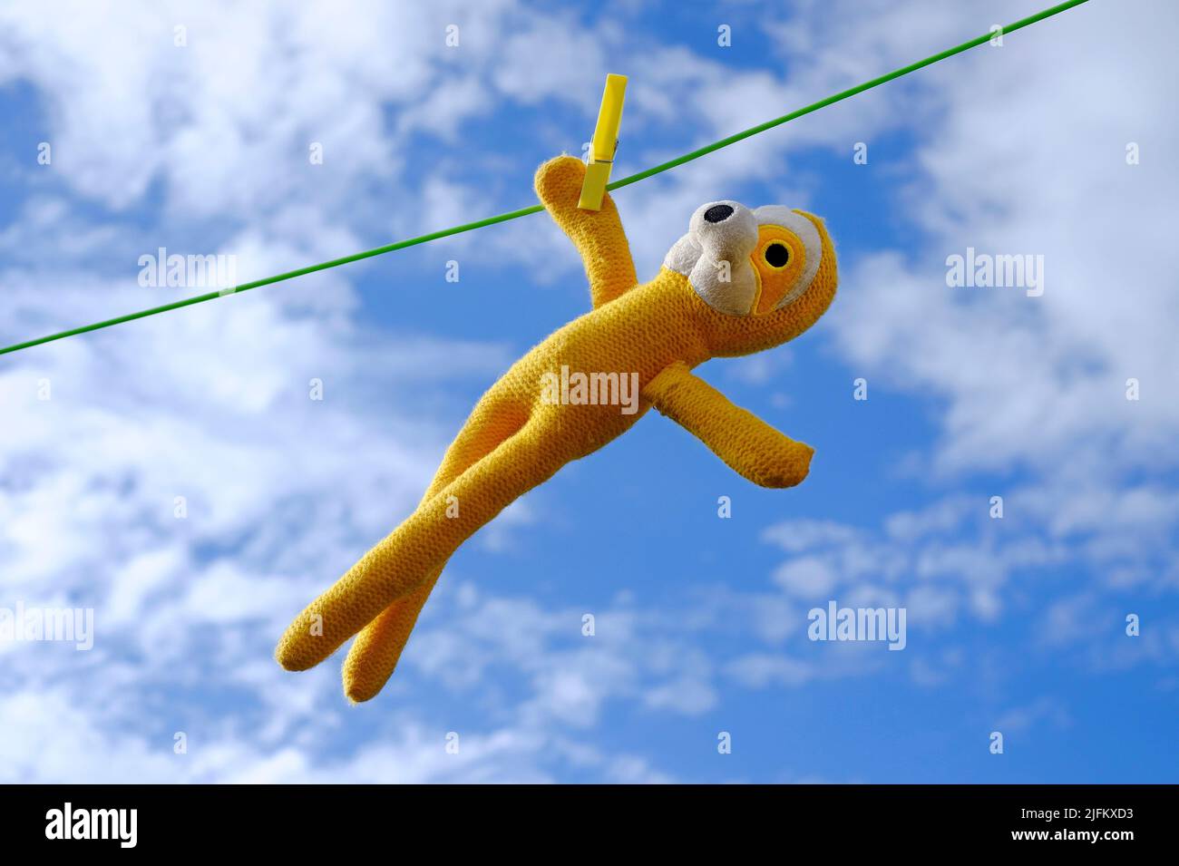 hombre de juguete amarillo colgando de la línea de ropa sobre fondo azul cielo Foto de stock
