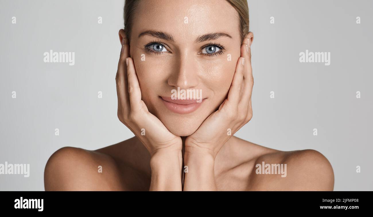 Cuidado de la piel. Mujer hermosa con piel facial sana que toca manos piel facial hidratada, sobre fondo gris claro. Alta calidad Foto de stock
