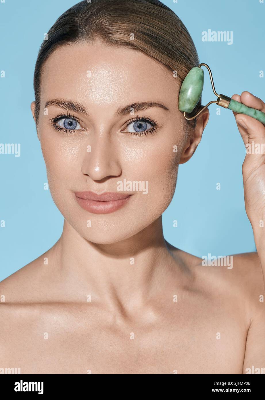 Retrato de una mujer adulta con rodillo de jade o rodillo para piedras para el procedimiento de elevación facial Foto de stock