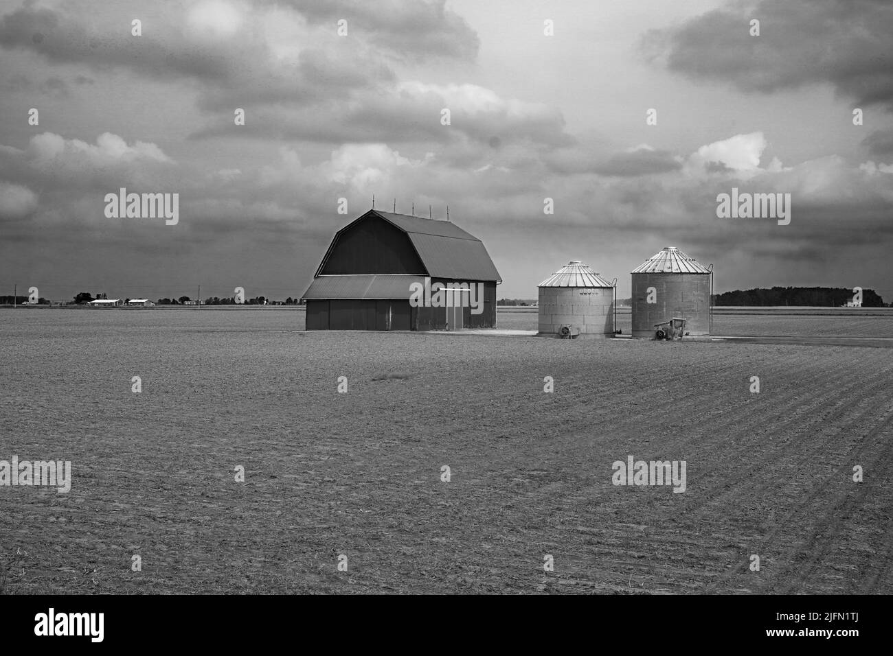 Escena agrícola en blanco y negro de un granero y dos silos rodeados por un campo recién arado en Ohio Foto de stock