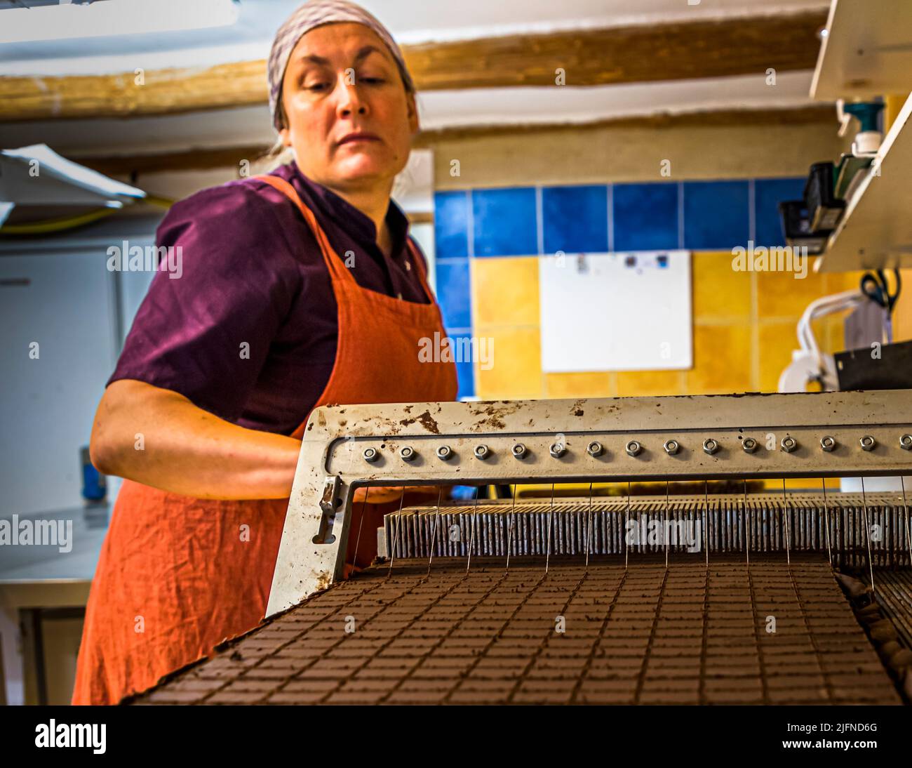 Empleado de Chocolaterie Frigoulettte en Beaufort-sur-Gervanne (Die, Francia) cortando pralinés de turrón. Die, Francia Foto de stock