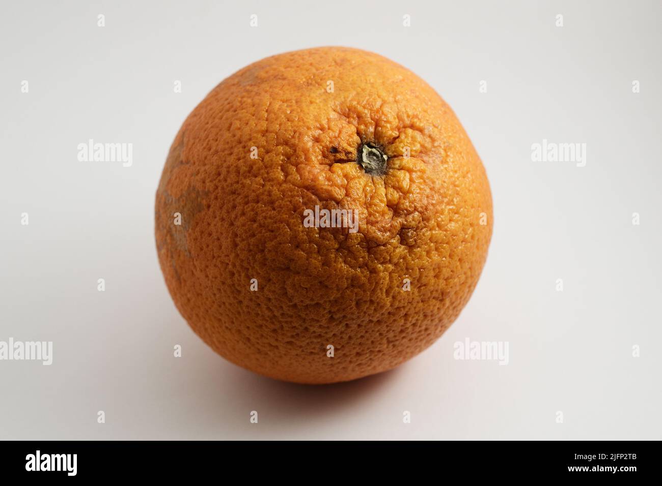 una naranja con una textura de cáscara pronunciada sobre un fondo blanco Foto de stock