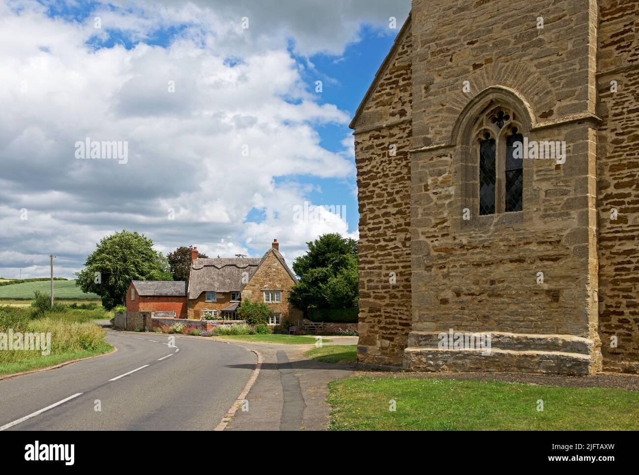 Casa de campo con techo de paja y All Saints Church en el pueblo de Sutton Bassett, Northampton, Inglaterra, Reino Unido Foto de stock
