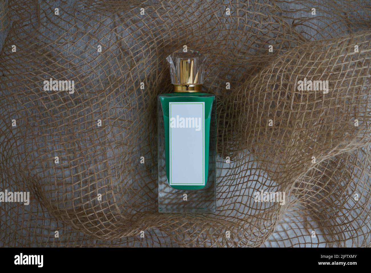 Frasco de perfume de fragancia verde con rectángulo blanco y tapa dorada, sobre un fondo blanco de madera y perfume de arpillera Mockup. Y renderizado 3D Foto de stock