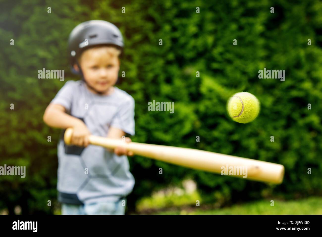 niño golpeando la pelota de tenis con el bate de béisbol en el patio trasero de su casa Foto de stock