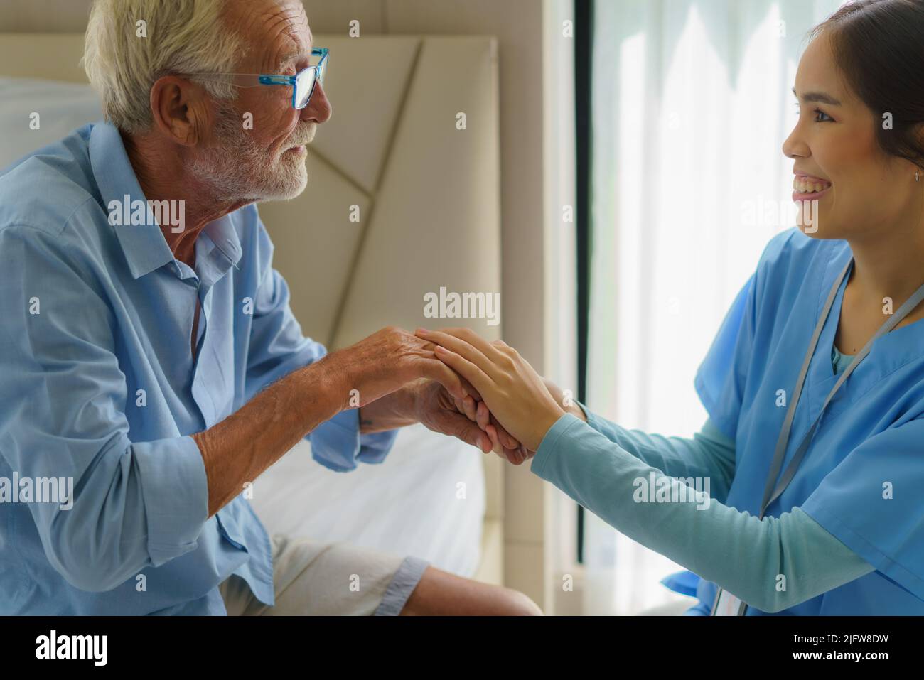 Enfermera asiática de pie en una cama de la casa junto a un hombre mayor que ayuda las manos, el cuidado. Atención al paciente de edad avanzada y estilo de vida de salud, concepto médico. Foto de stock