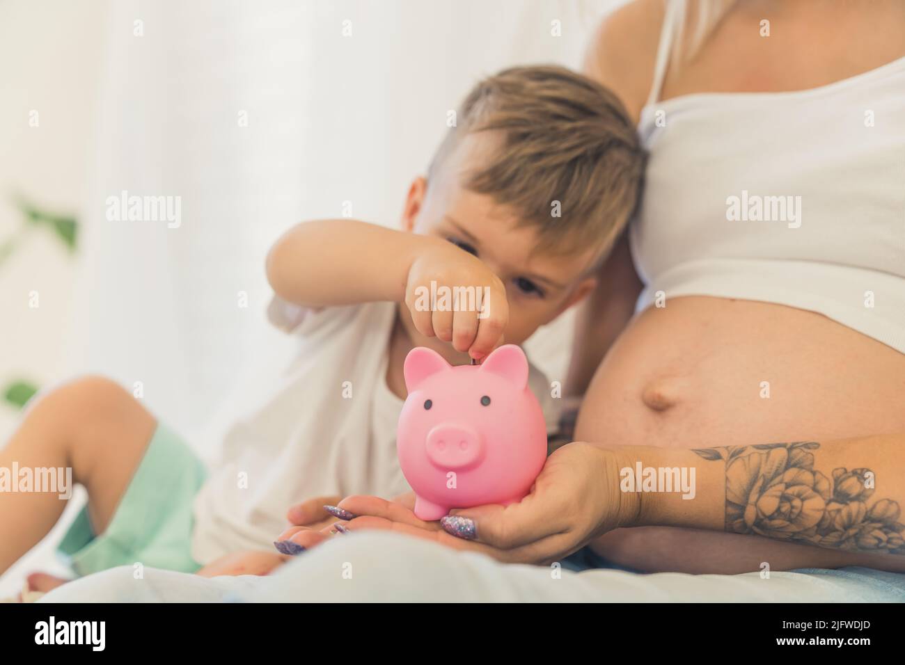 Pequeño lindo muchacho caucásico poniendo dinero en la rivera de cerdos con su madre embarazada. Fotografía de alta calidad Foto de stock