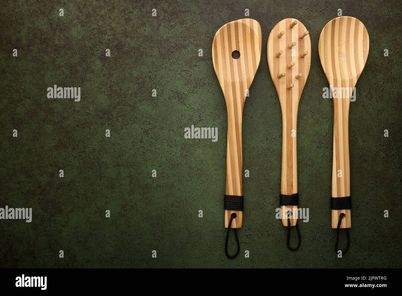 Cocinar cucharas de bambú sobre fondo verde oscuro, vista superior Foto de stock