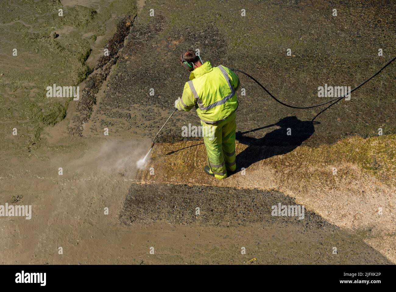 Penzance, Cornualles, Inglaterra, Reino Unido. 2022. Hombre usando una lavadora a presión en la marea baja para limpiar una rampa Penzance Harbour Foto de stock