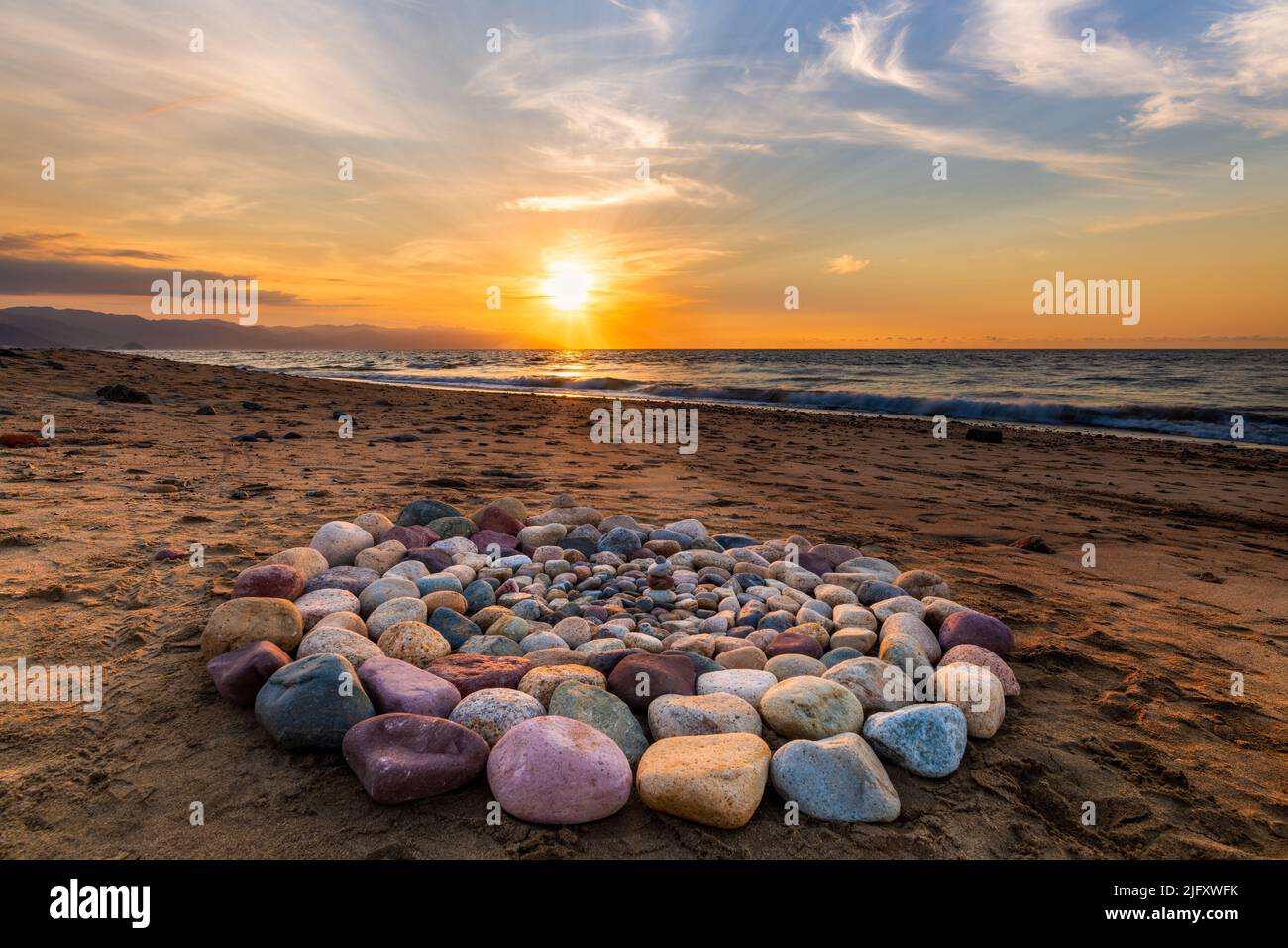Las piedras rituales para la ceremonia espiritual se organizan en un círculo durante la puesta de sol en la playa Foto de stock