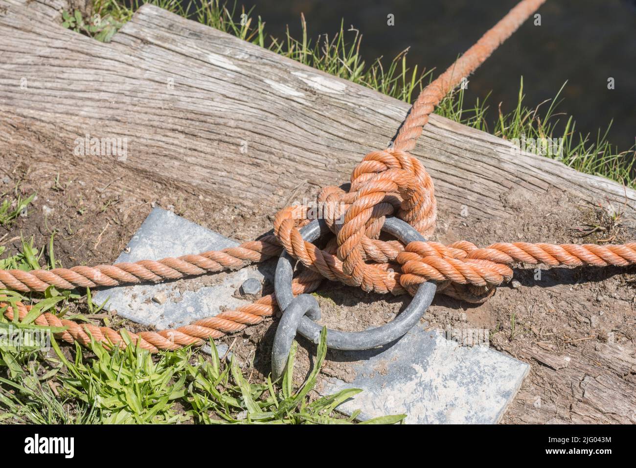 Muelle soleado con cuerda de amarre de barco unida a anillo de amarre de metal. Para las actividades de navegación y navegación en el Reino Unido, algo seguro, atado, atado. Foto de stock
