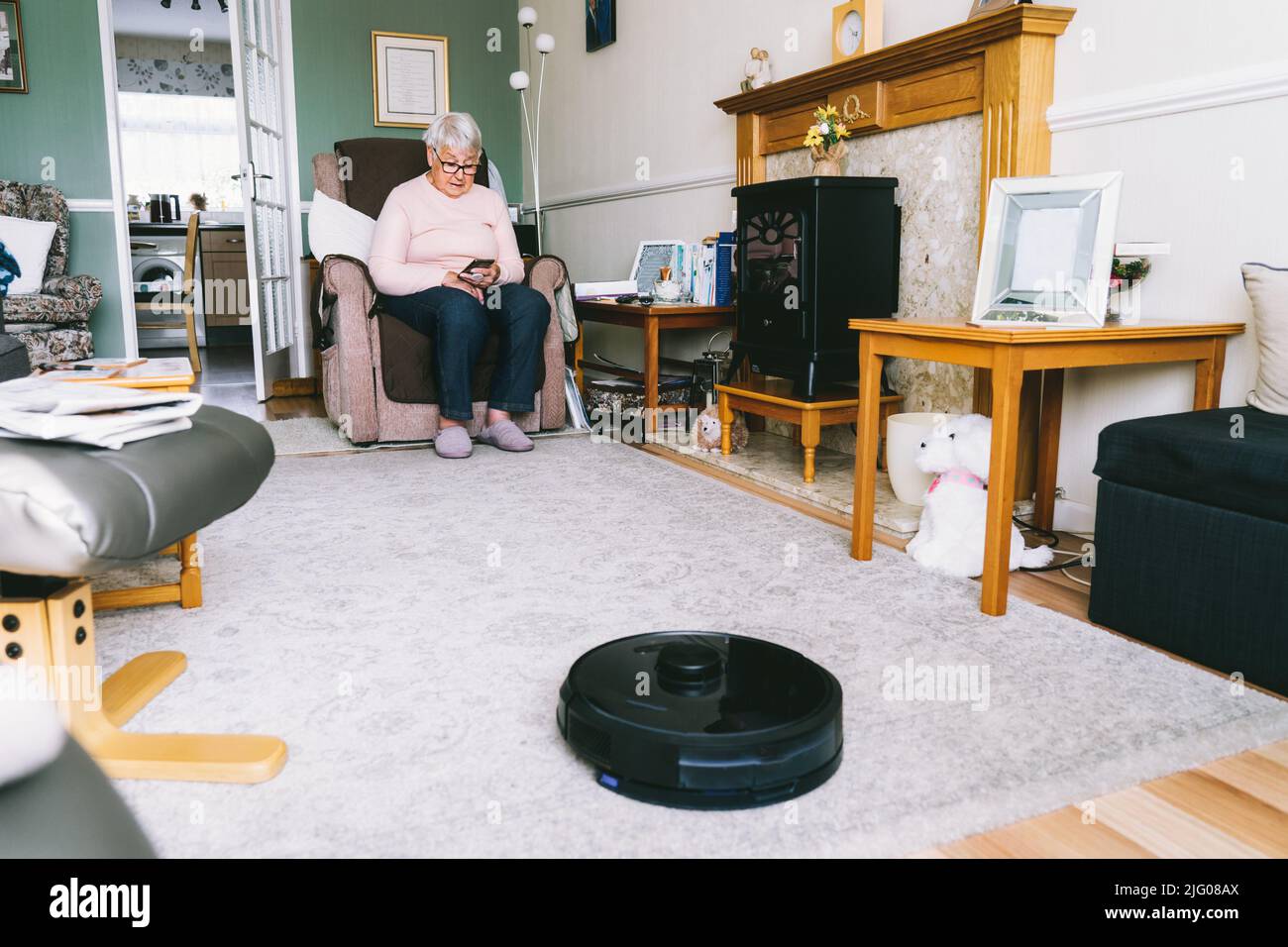 Mujer relajándose en el sofá mientras robot aspirador haciendo quehaceres  domésticos