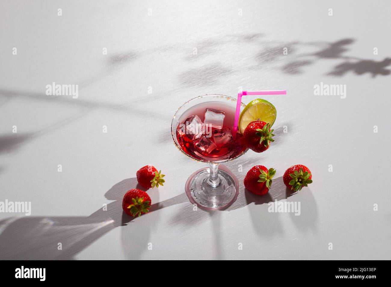 Delicioso cóctel. Bebida roja para fiestas en un elegante vaso de vidrio con cubitos de hielo, fresa y lima sobre fondo negro, Foto de stock