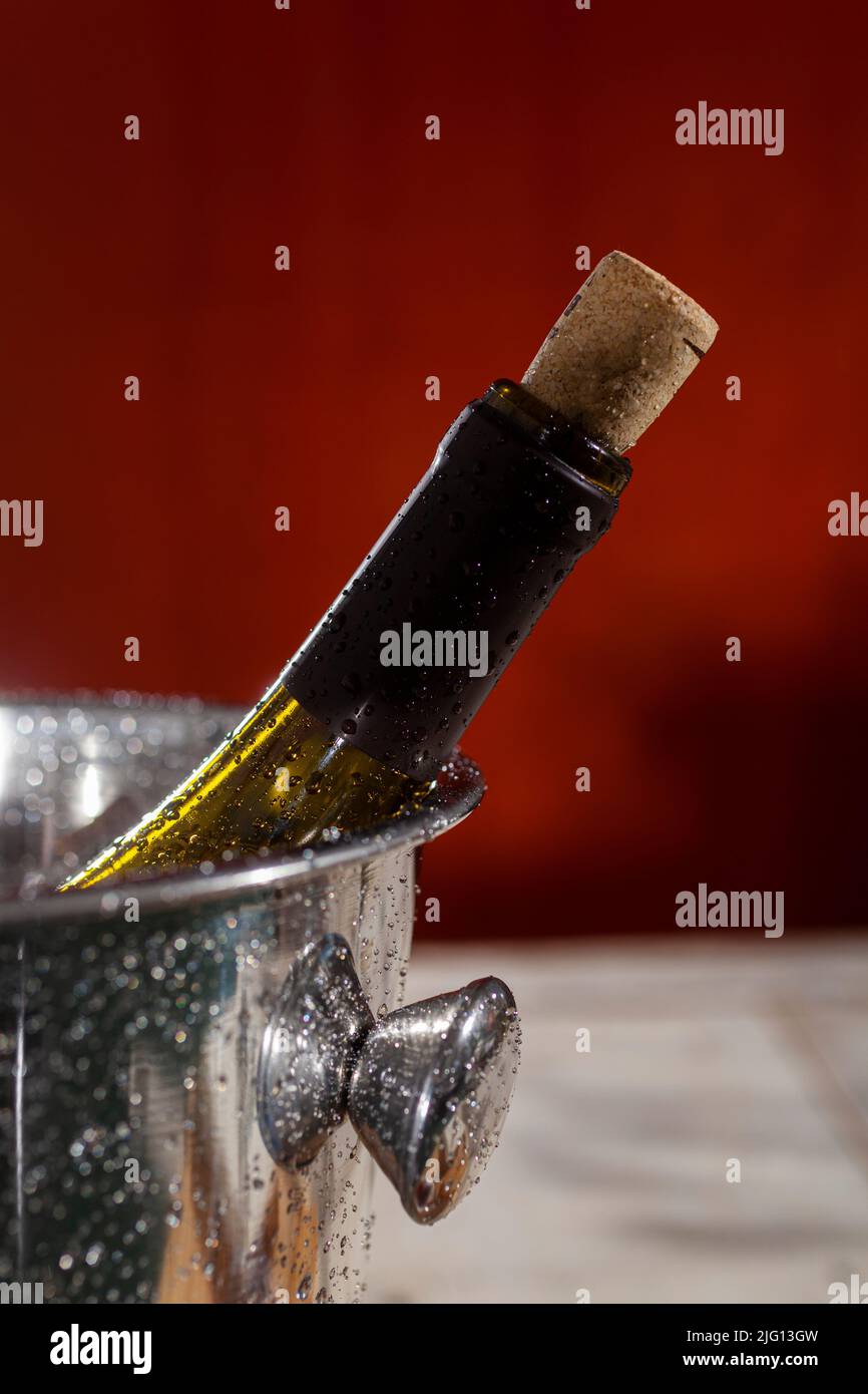 Primer plano del cuello de una botella de vino con un corcho en gotas de agua sobre fondo rojo Foto de stock