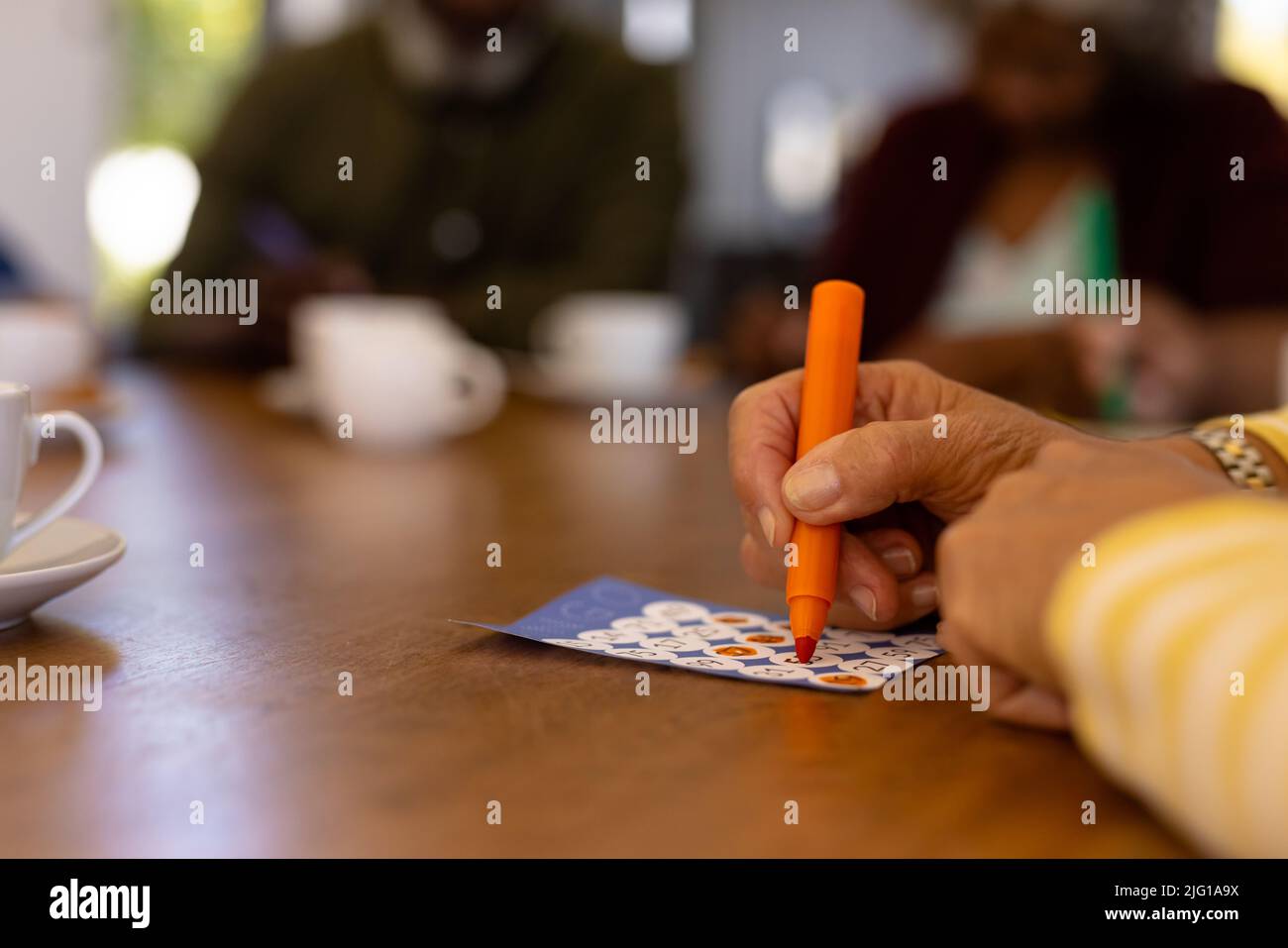 Mano recortada de una mujer mayor biracial marcando números en la tarjeta de bingo sobre la mesa en un hogar de ancianos Foto de stock