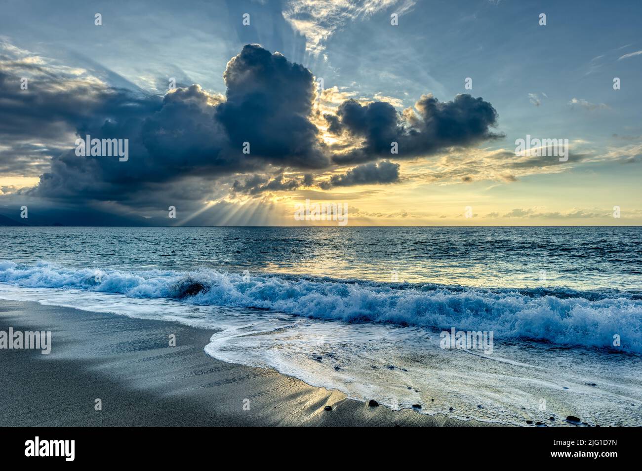 Los brillantes rayos del sol están reventando a través de las nubes en un paisaje al atardecer en el océano Foto de stock