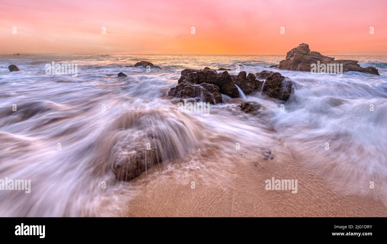 El agua fluye a través de las rocas del océano en la resolución alta del amanecer Foto de stock