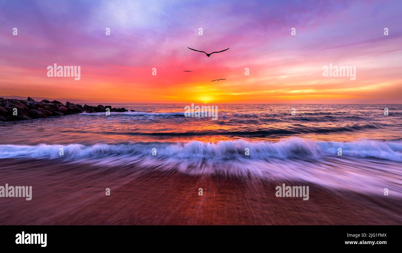 Puesta de sol del paisaje oceánico con aves volando hacia Un colorido cielo romántico Foto de stock
