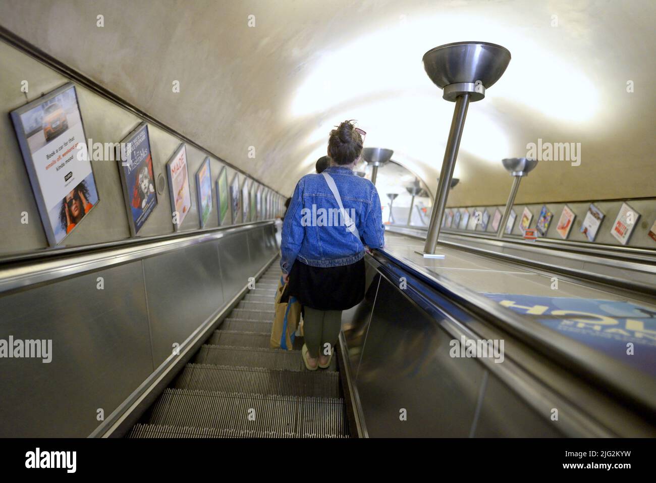 Londres, Inglaterra, Reino Unido. Mujer en una estación de metro de Londres por una escalera mecánica Foto de stock