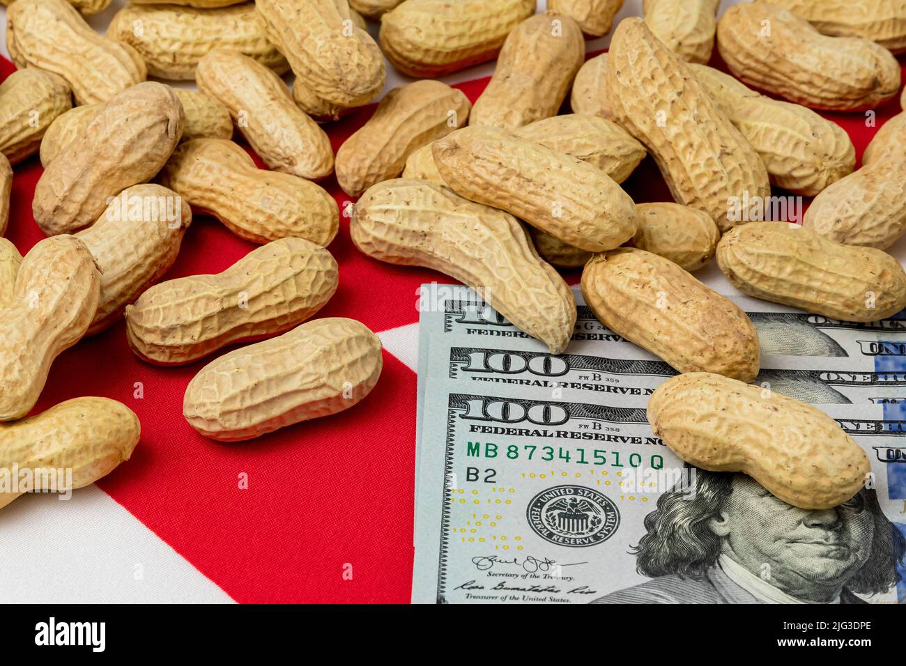 Cacahuetes en concha en la bandera de Alabama con billetes de 100 dólares. Concepto de cultivo de cacahuetes, comercio, aranceles y precios de mercado. Foto de stock