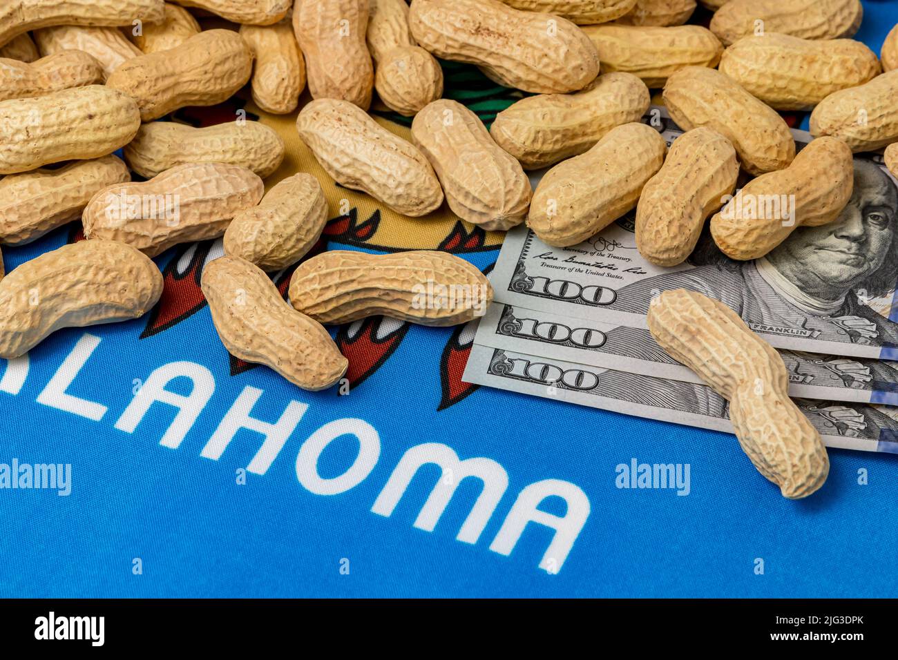Cacahuetes en concha en la bandera de Oklahoma con billetes de 100 dólares. Concepto de cultivo de cacahuetes, comercio, aranceles y precios de mercado. Foto de stock
