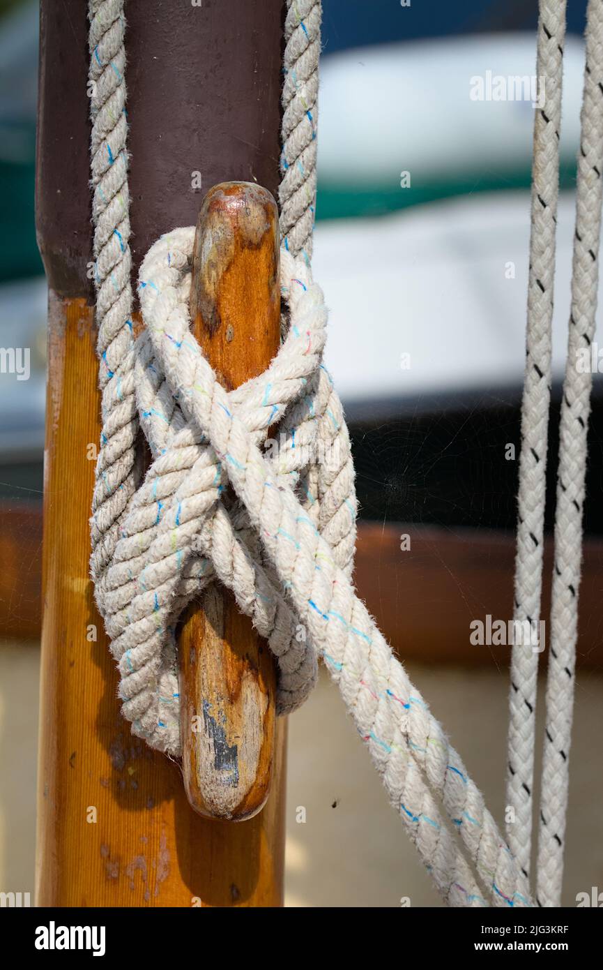 Figura de ocho enganches de garras que aseguran Un halyard alrededor De una cala de madera en un mástil de madera de un barco de vela, Reino Unido Foto de stock