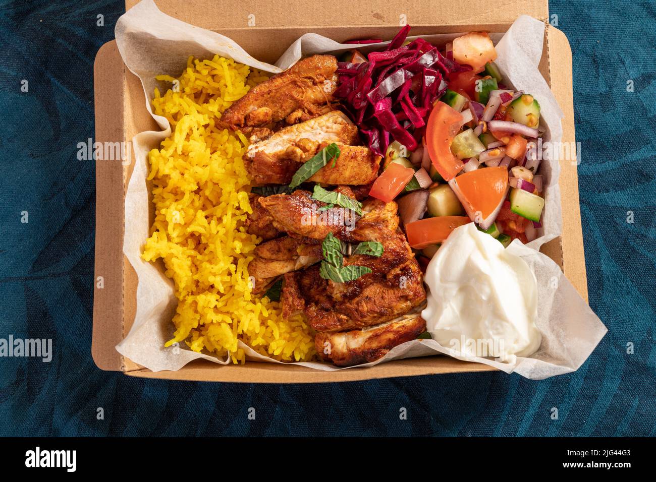 Comida tradicional mediterránea oriental para llevar de pollo a la parrilla, arroz amarillo, ensalada fresca y yogur en envases de cartón Foto de stock