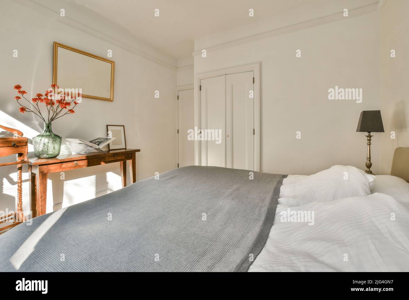 Moderno diseño interior de la casa pequeño dormitorio con paredes blancas y cama suave y acogedora y estantes de estilo minimalista con luz natural Foto de stock