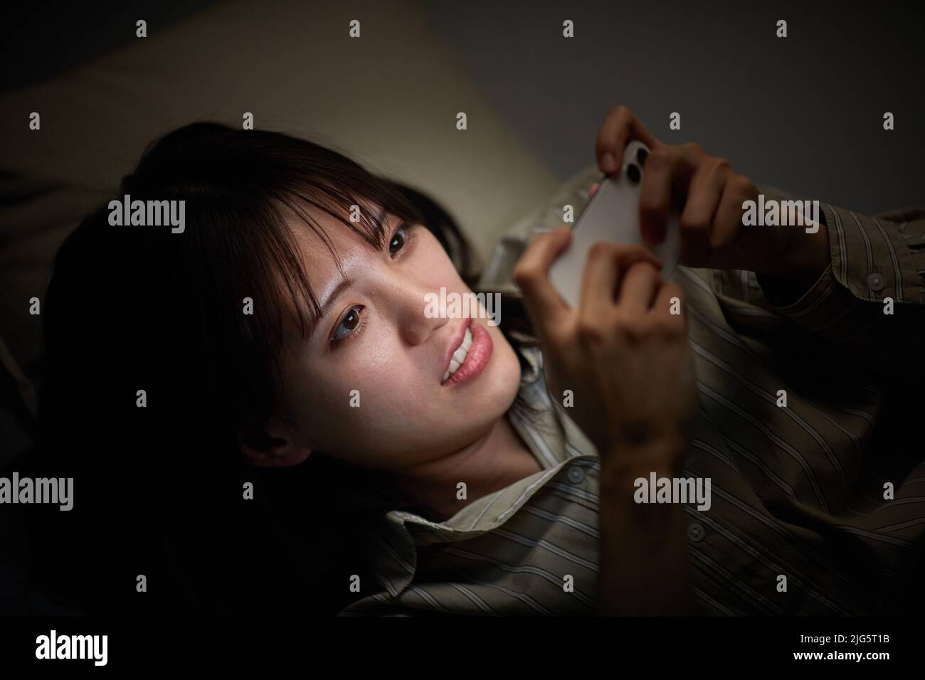 Mujer japonesa usando un smartphone en la cama Foto de stock