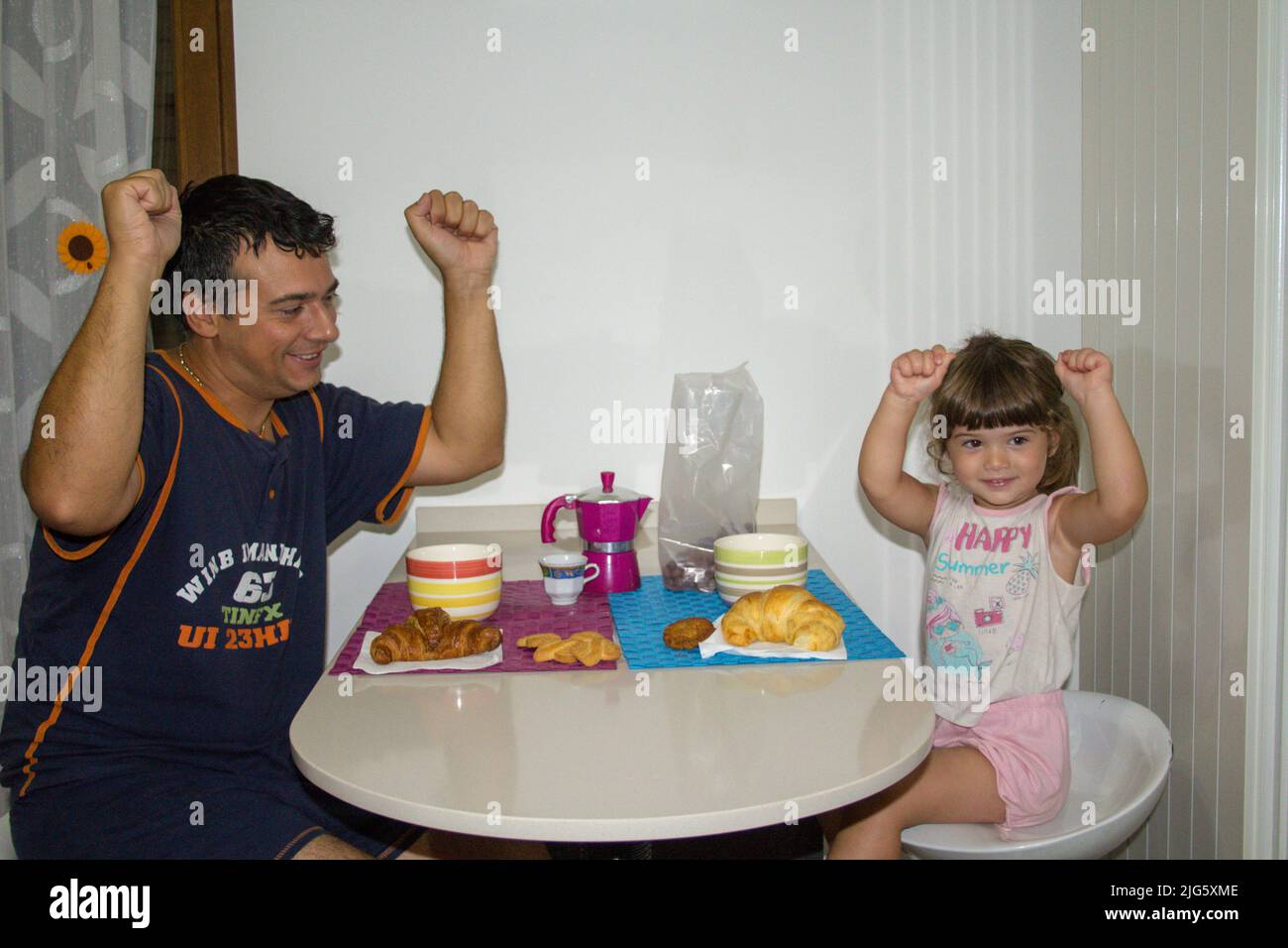 Imagen de un padre con su hija con los brazos levantados y sonriendo mientras desayunaba por la mañana Foto de stock