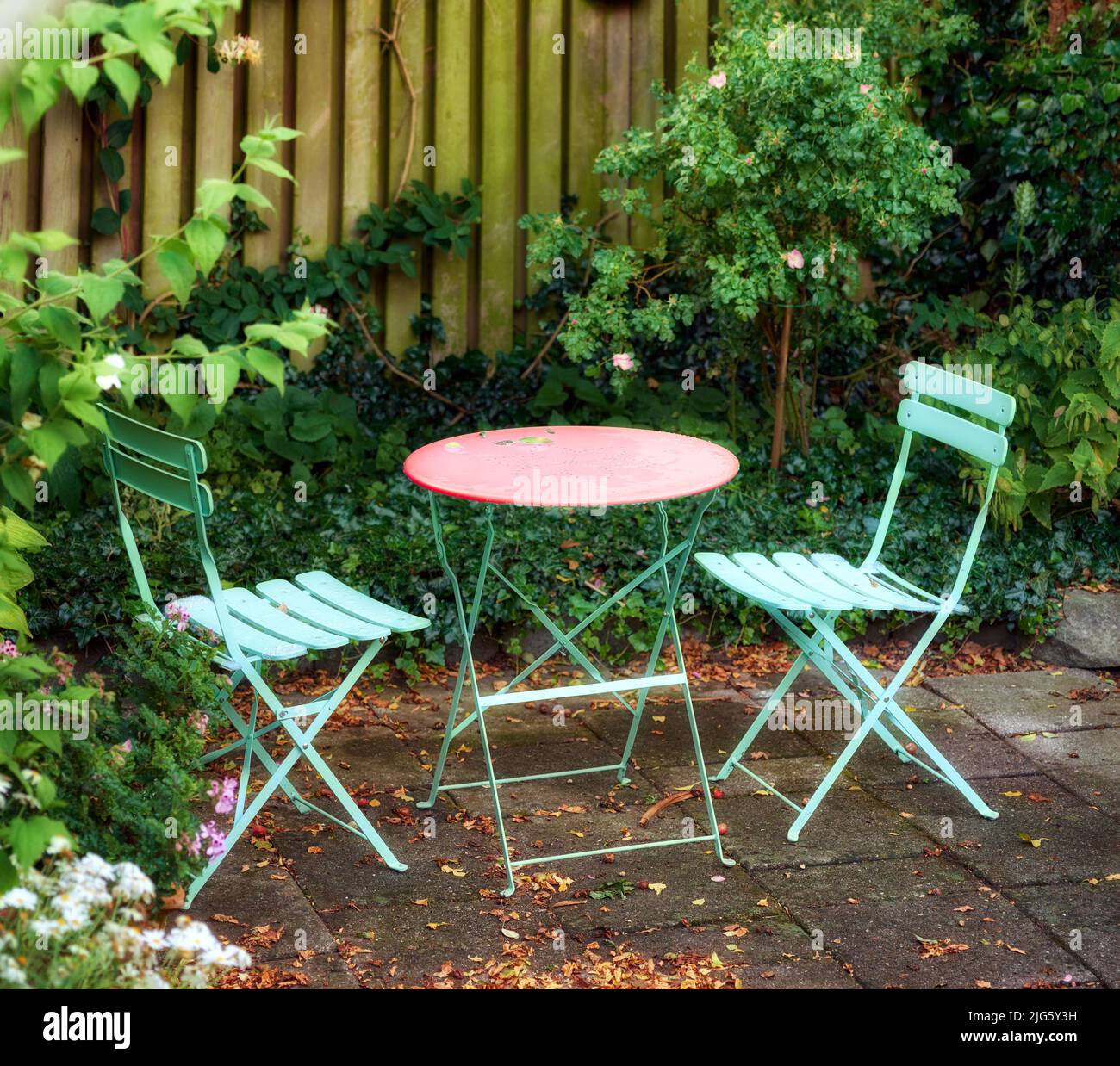 Sillas y mesa de metal con plantas en flor en un parque o patio privado al aire libre. Tranquilo paisaje verde exuberante y relajante lugar en un jardín Foto de stock