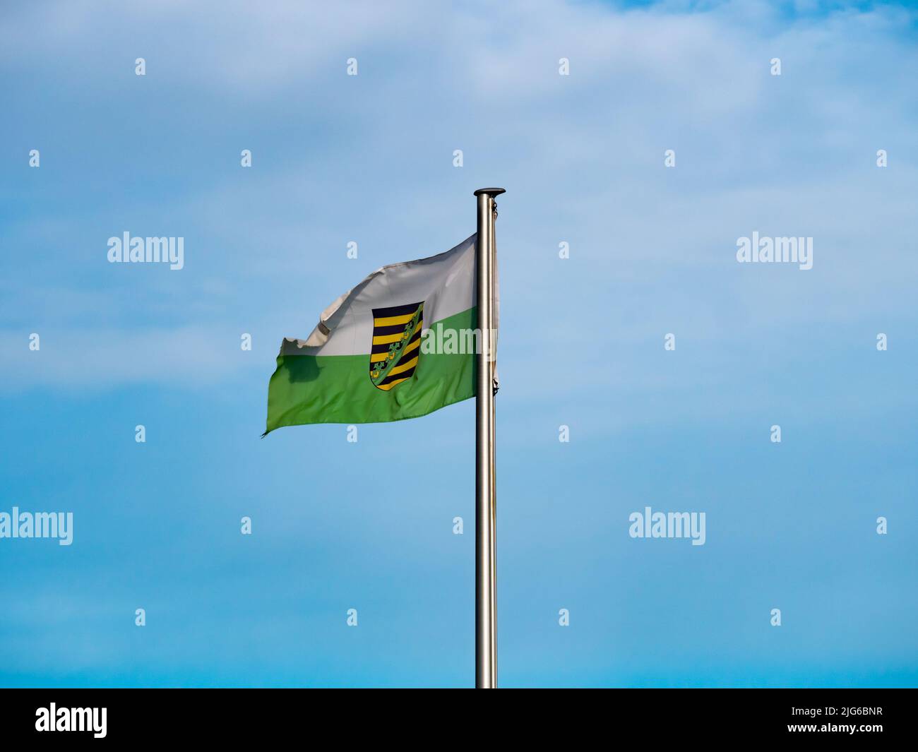 Bandera de Sajonia con escudo ondeando en el viento. Cielo azul en el