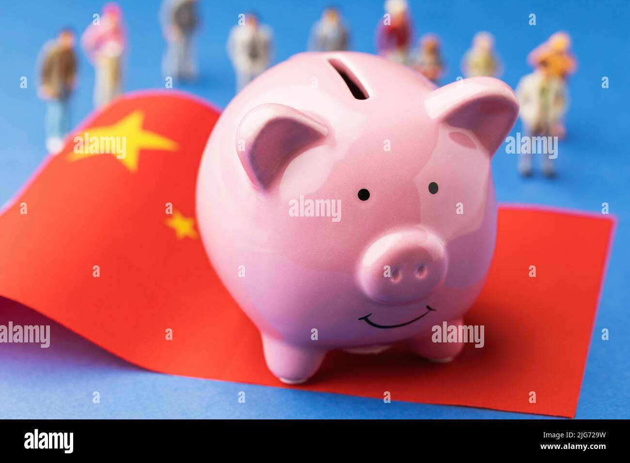 Banco de cerdos, bandera china y juguetes de plástico sobre un fondo de color, un concepto sobre el tema de los ingresos en China Foto de stock