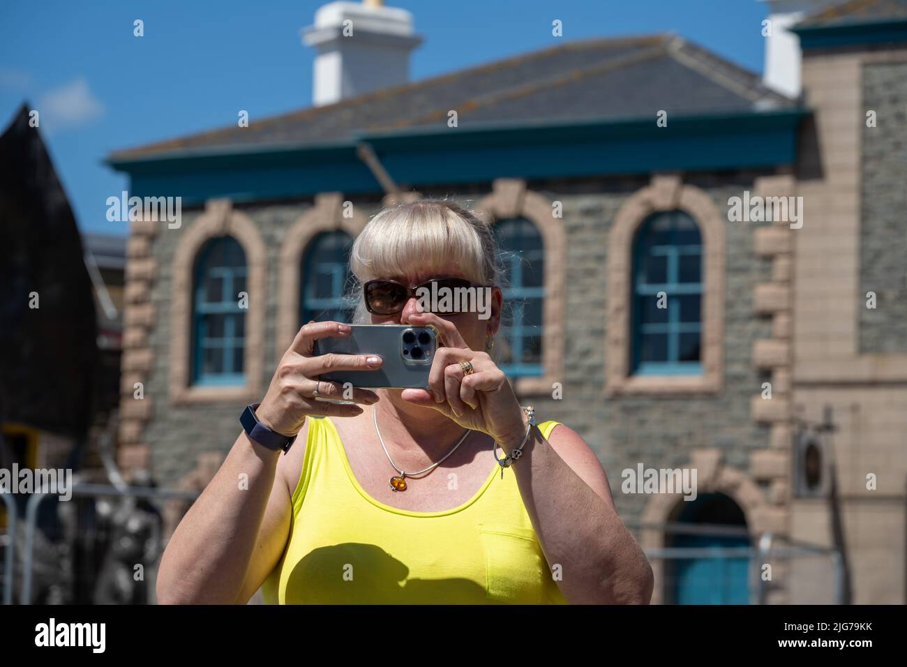 Turista adulta con gafas de sol y una parte superior amarilla tomando fotografías en un teléfono móvil durante sus vacaciones en verano. Foto de stock