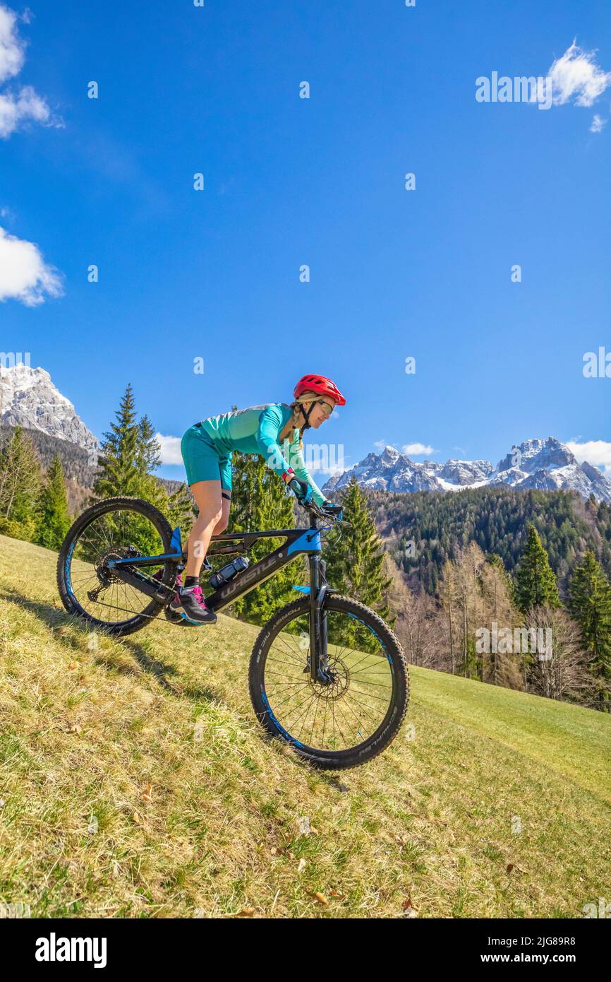 Mujer rubia caucásica con ropa técnica deportiva montando una bicicleta electrónica en las montañas, dolomitas, Belluno, Véneto, Italia Foto de stock