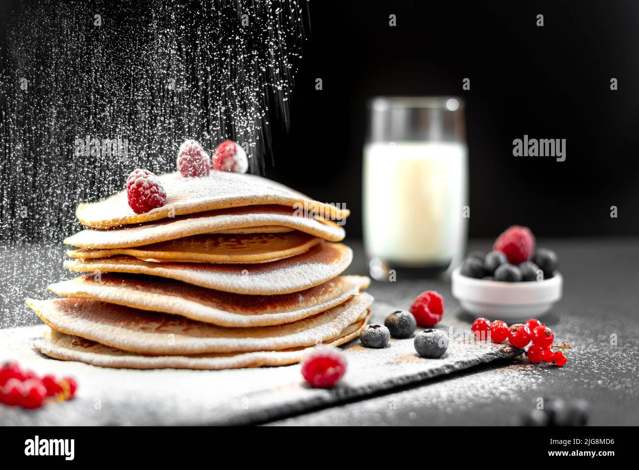 Grandes panqueques americanos sobre un fondo oscuro. Desayuno europeo. Chef espolvorea panqueques con azúcar en polvo sobre fondo negro. Comida para el desayuno Foto de stock